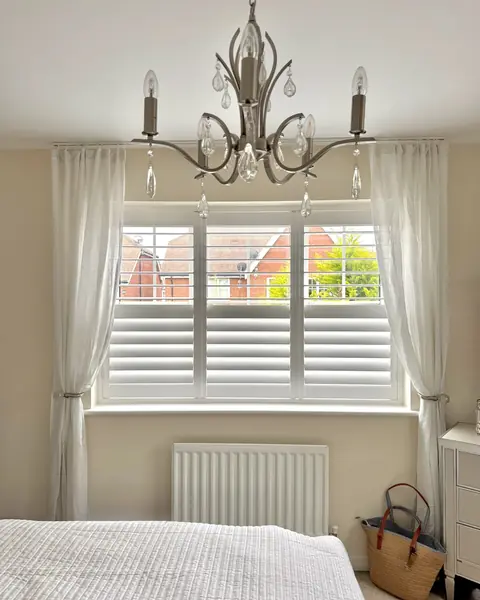 Hardwood shutters on a bedroom window beneath a chandelier