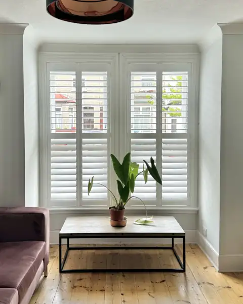 Hardwood shutters on a wide living room window, fitted after a home survey