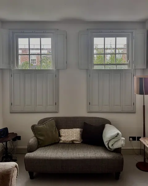 Tier on tier hardwood shutters on a pair of sash windows above a sofa